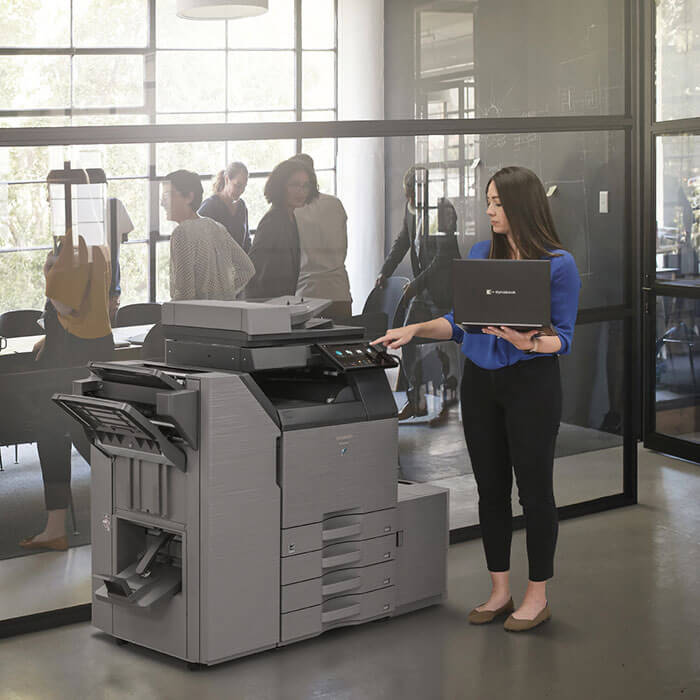 Woman holding laptop and using the large printer in office