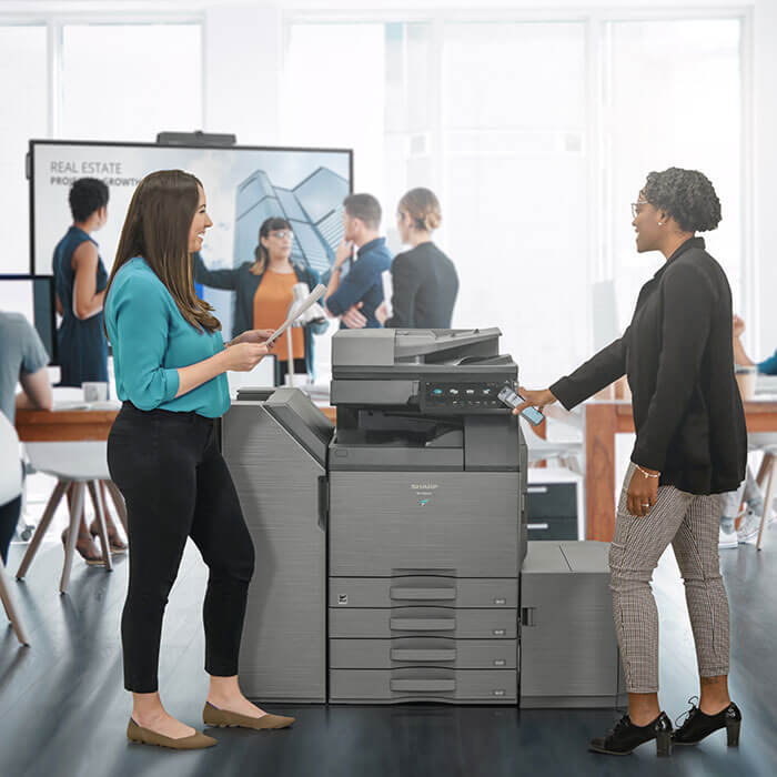 women smiling around large printer in office