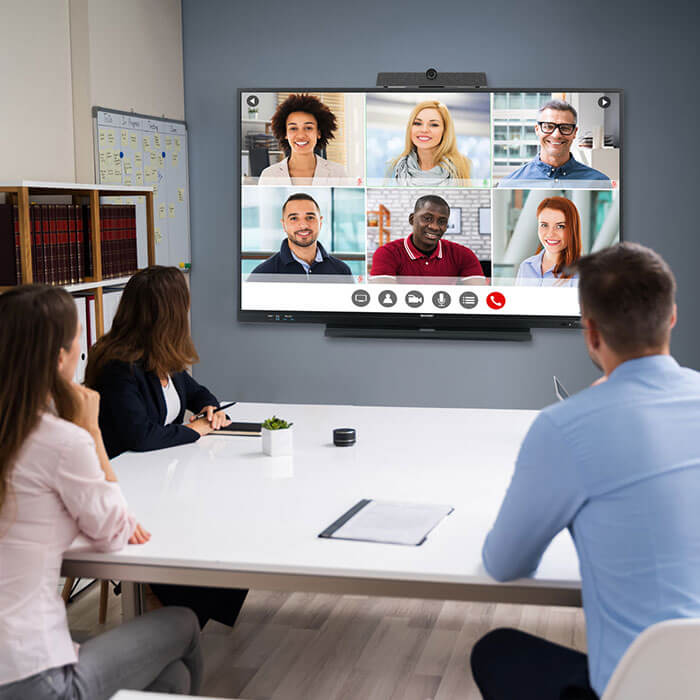 workers seated at table for call with video conferencing system