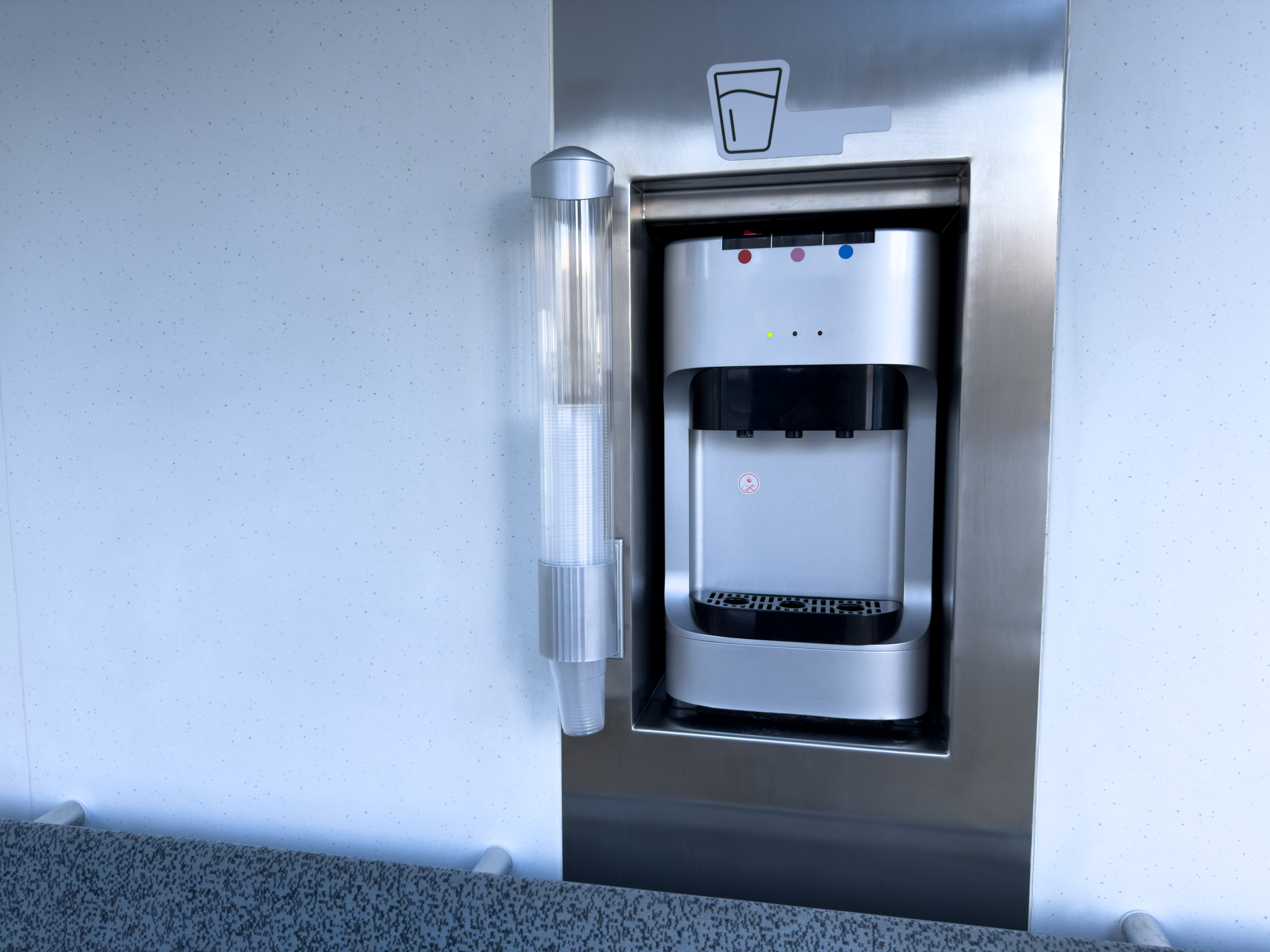 Stainless steel water dispenser with paper cup holder inside modern public transport. Comfortable passenger area with seating and hydration access for daily commuters